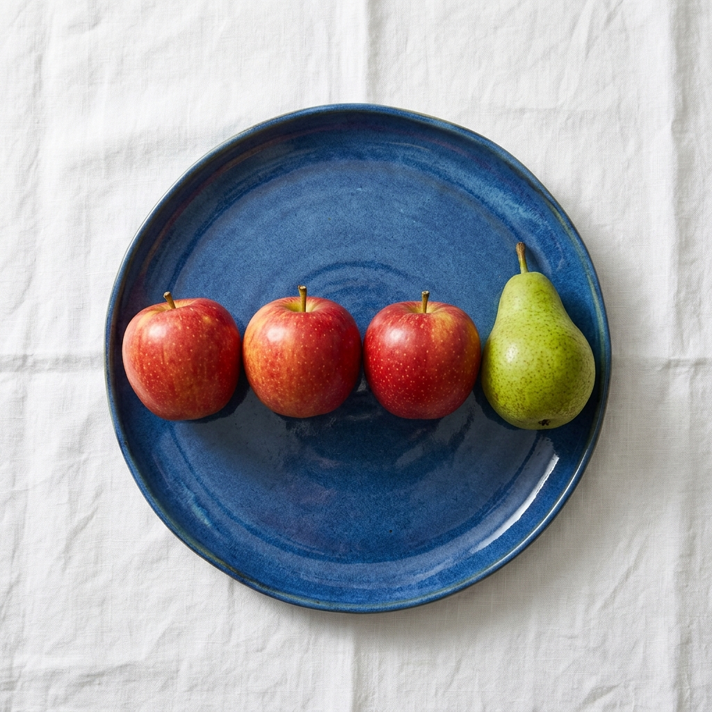 Nano Banana 2.1: Three red apples and one green pear arranged in a single row on a blue plate, top-down view, white tablecloth