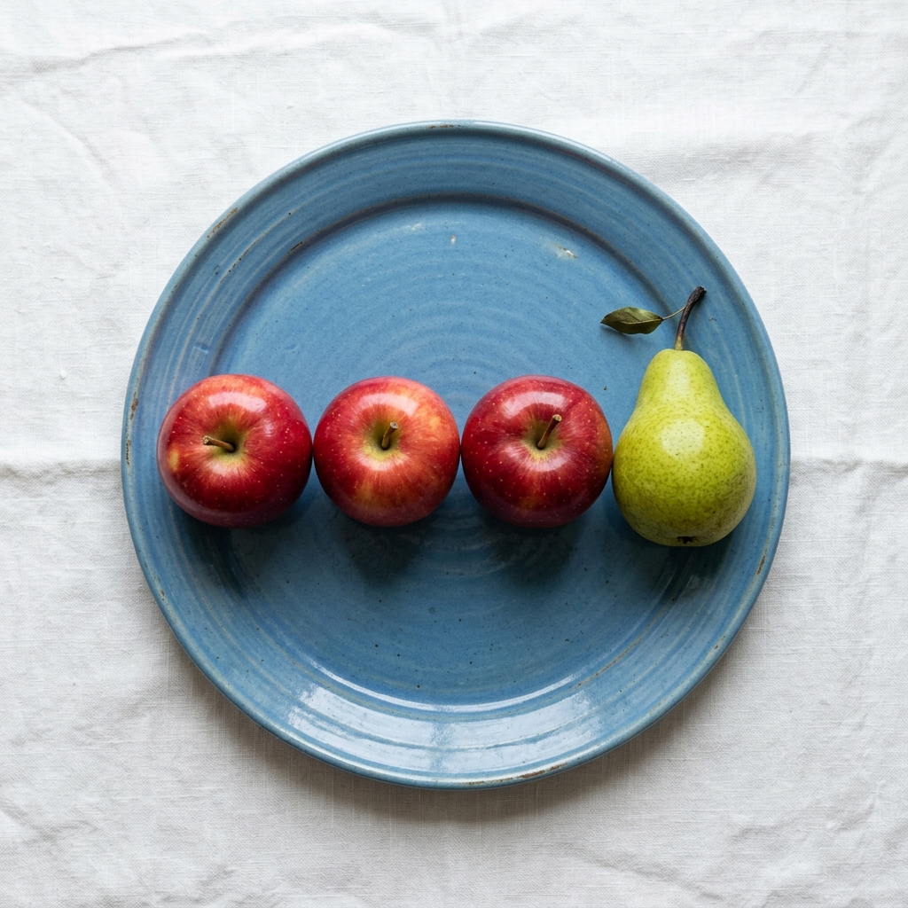 Nano Banana 2: Three red apples and one green pear arranged in a single row on a blue plate, top-down view, white tablecloth