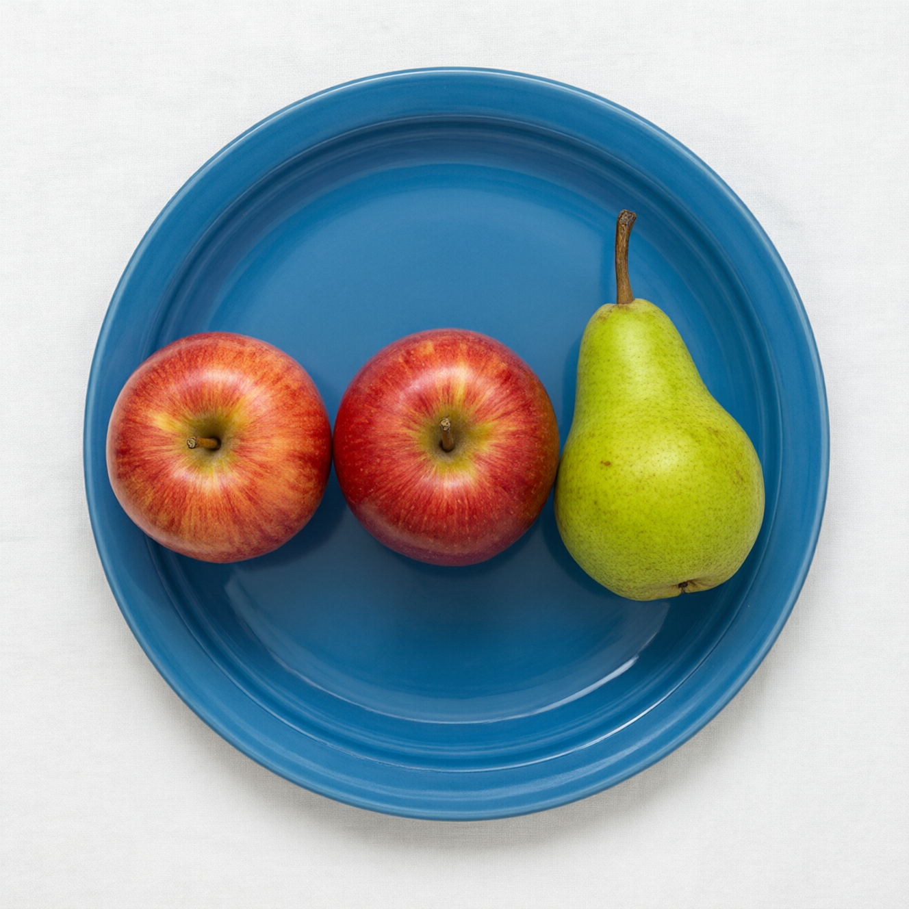 Qwen Image 3.0: Three red apples and one green pear arranged in a single row on a blue plate, top-down view, white tablecloth