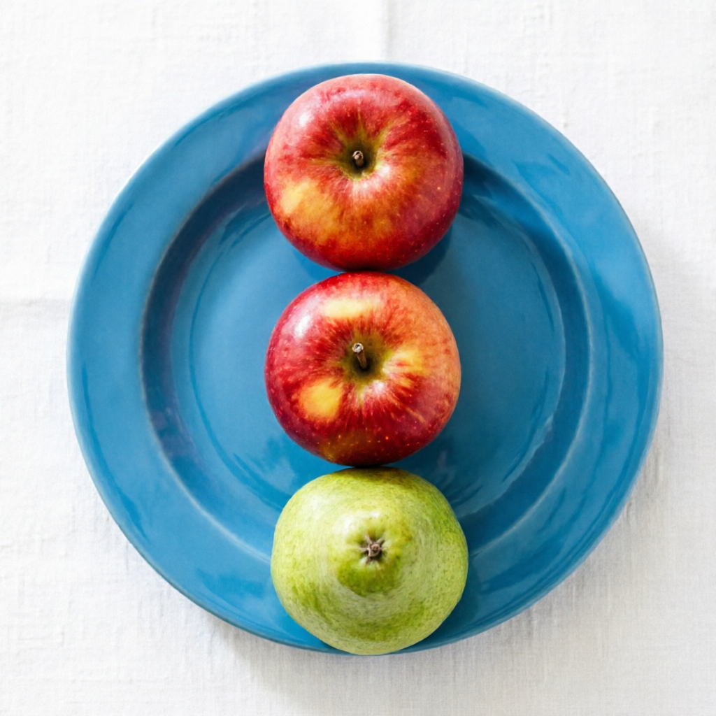 Qwen Image 2.0: Three red apples and one green pear arranged in a single row on a blue plate, top-down view, white tablecloth