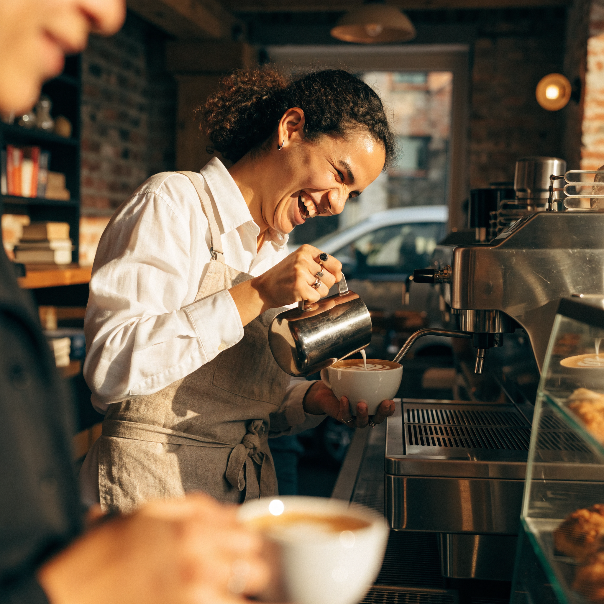Recraft V4.1 Pro: A barista in a linen apron laughing while pouring latte art, warm cafe interior, shallow depth of field, candid editorial style